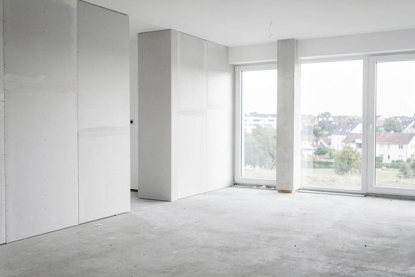 Heller Innenraum im Ausbau: fertige Trockenbauwände, glatter Estrich, bodentiefe Fenster.